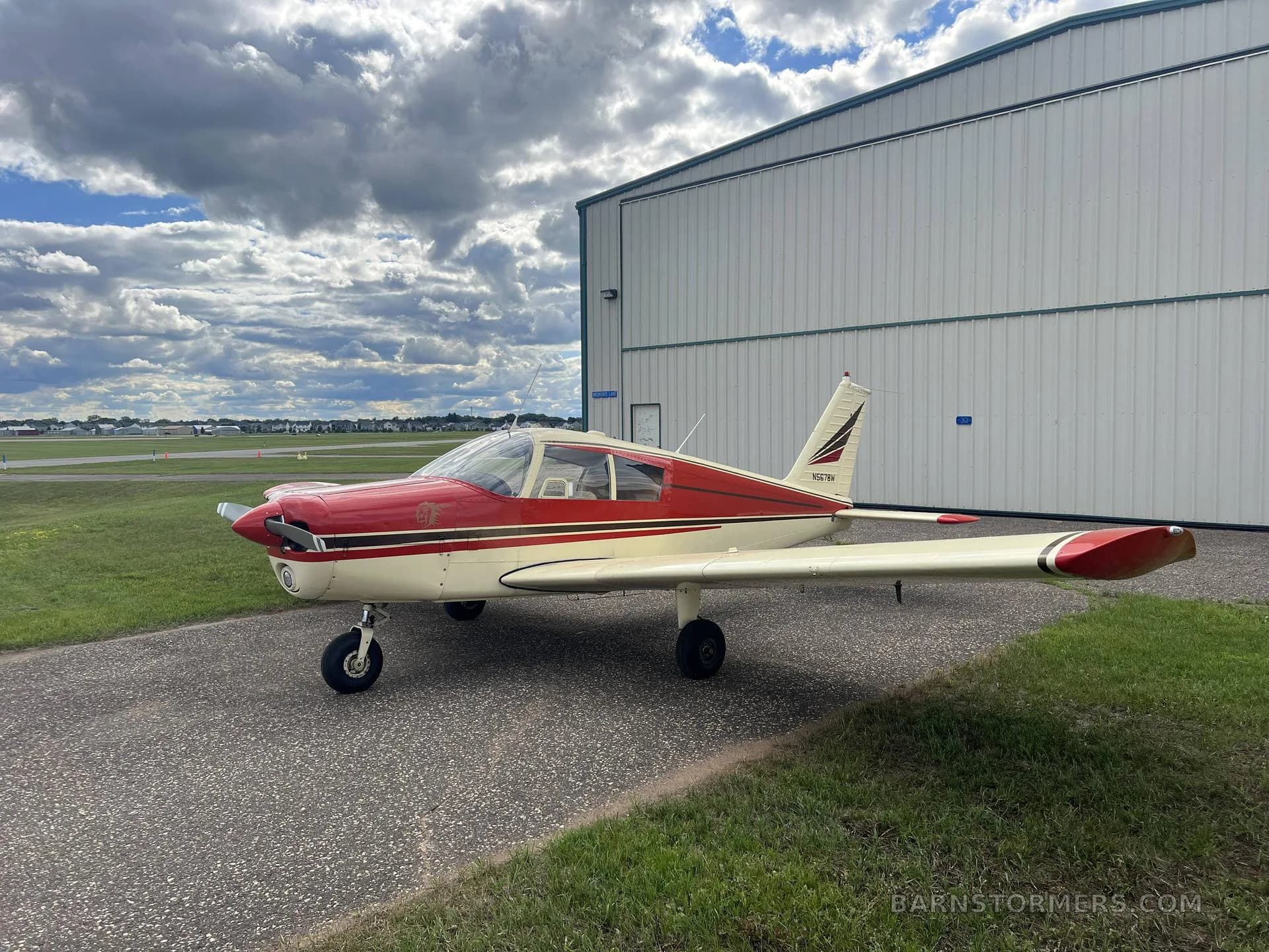 A red and cream single-engine propeller aircraft (N5678W) parked on an asphalt ramp beside a hangar.