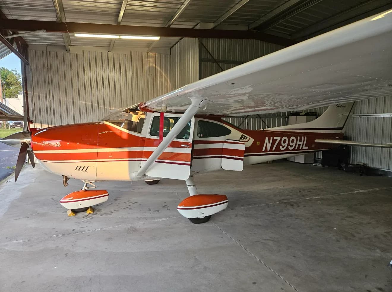 A Cessna Skylane in a hangar with its door open.
