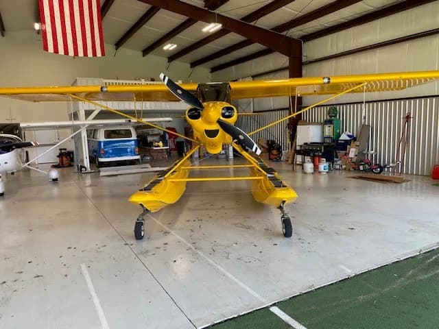 Front view of a yellow Carbon Cub floatplane with a propeller, parked inside a hangar.