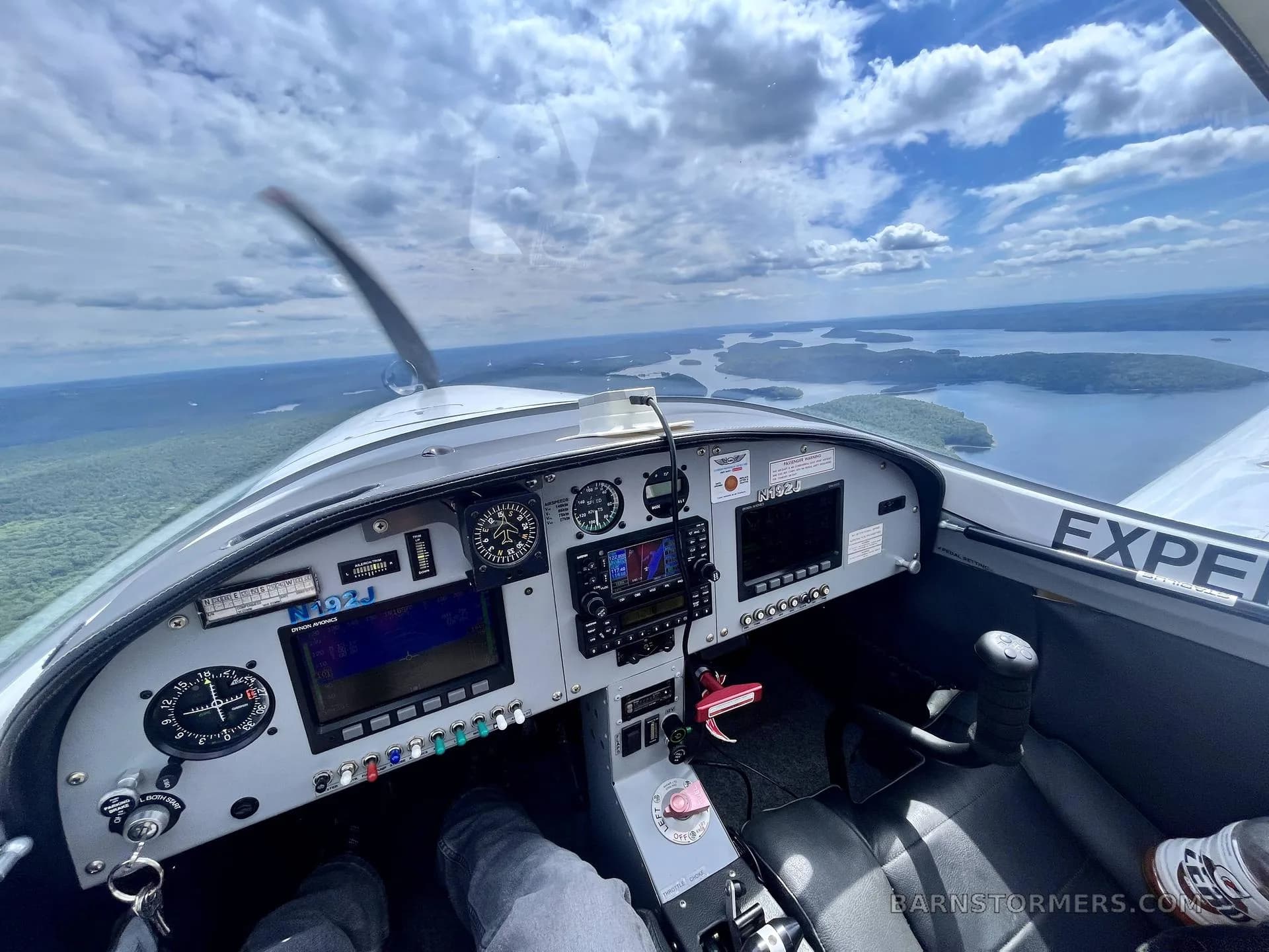 A pilot's view from the cockpit of an aircraft flying over a scenic landscape with numerous lakes and islands.