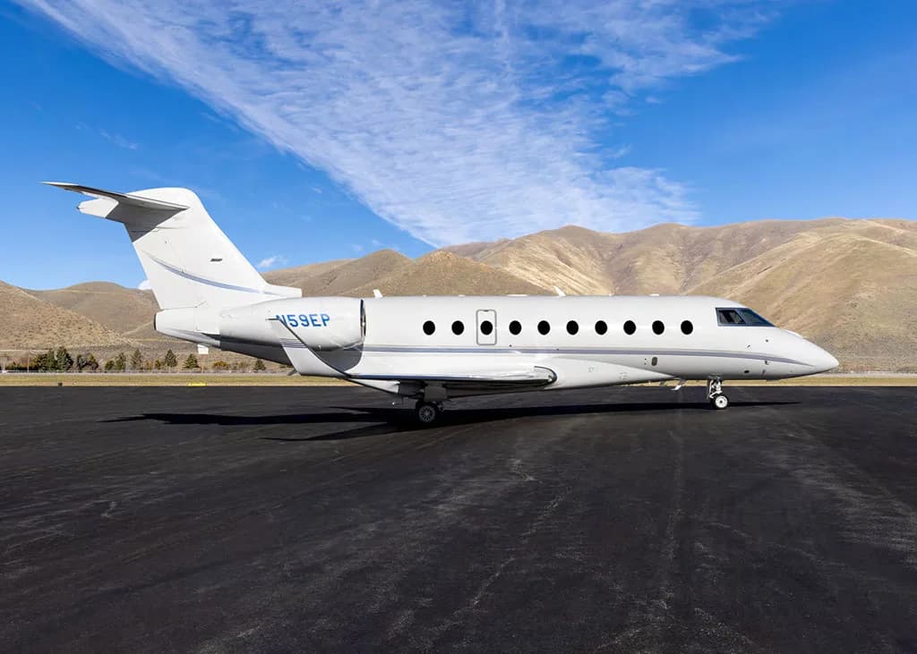 A white Gulfstream G550 business jet, tail number N59EP, is parked on an airfield under a blue sky.