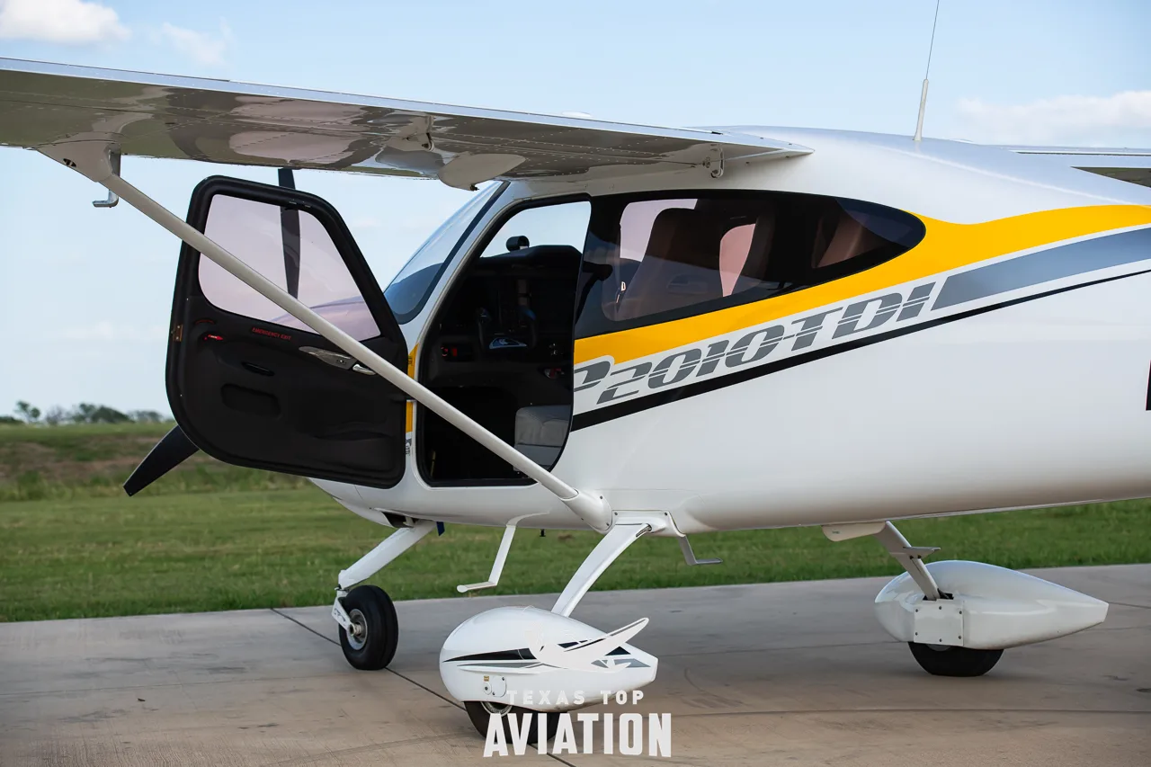 A close-up of the side of a white and yellow Tecnam P2010 TDI aircraft with the pilot's door open.