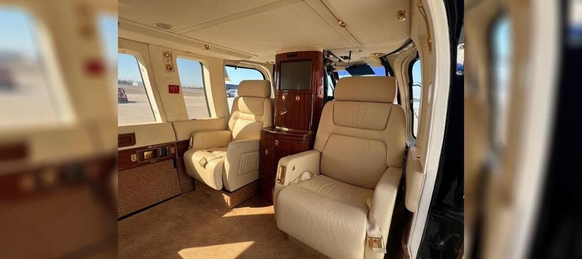 The interior of the helicopter features cream-colored leather seats and wood trim.