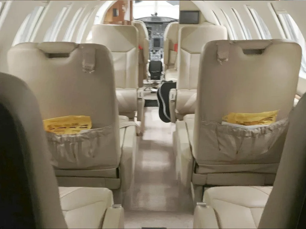 A view down the aircraft cabin aisle, showing rows of beige leather seats facing forward towards the cockpit.