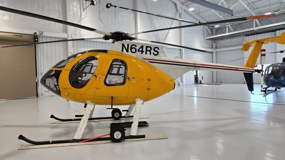 A yellow helicopter with tail number N64RS is parked in a brightly lit hangar.