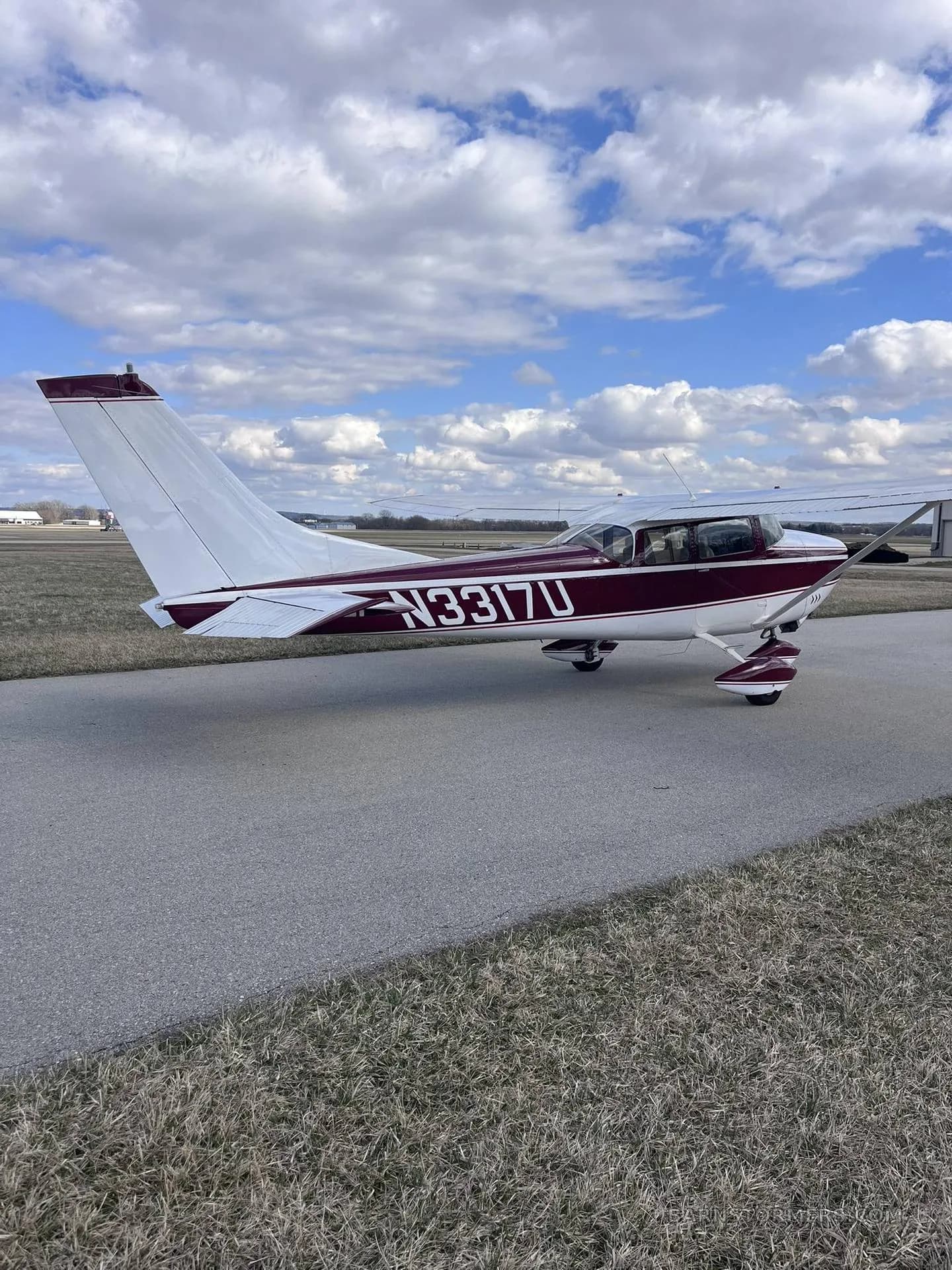 A maroon and white single-engine propeller aircraft (N3317U) viewed from the rear-side, parked on an asphalt taxiway.