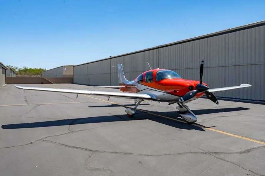 Three-quarter front view of a red and silver Cirrus SR22T aircraft (N566TT) parked on an airfield.
