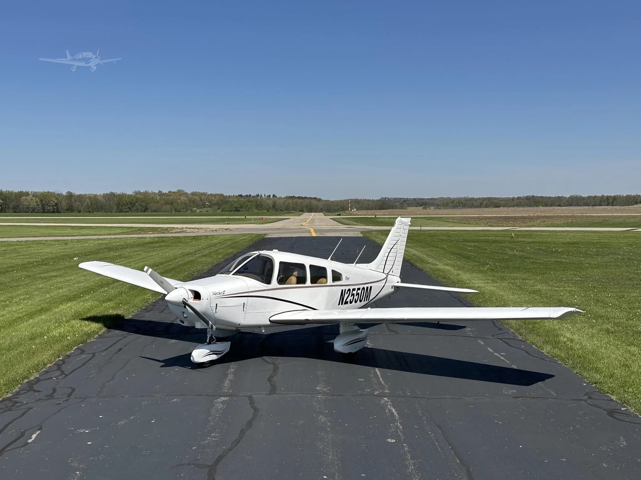A white Piper Cherokee aircraft, N2550M, with black stripes, parked on a runway with green grass and a clear blue sky.