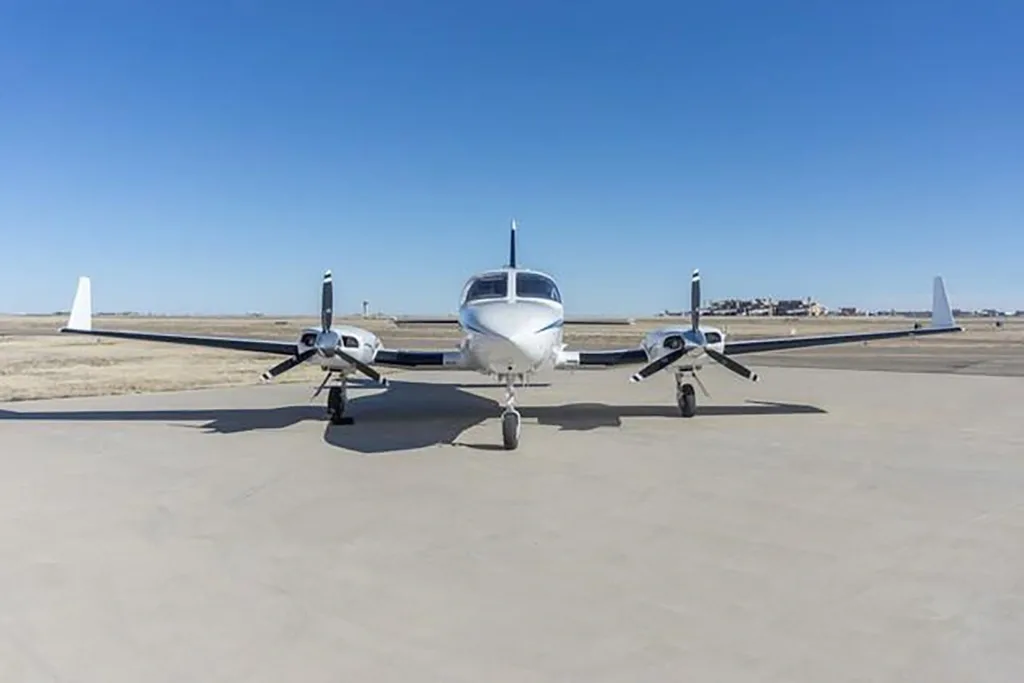 A wide head-on view of a white twin-engine Cessna 414 Chancellor aircraft with blue stripes on an airfield.