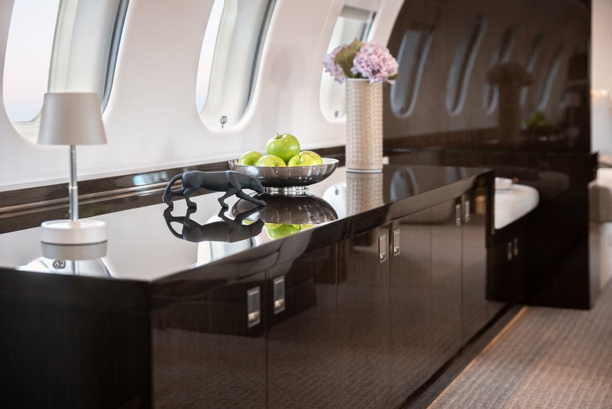 A dark wood cabinet with a bowl of green apples and a black panther statue in the aircraft cabin.