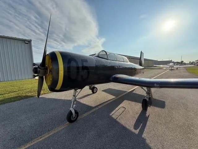 A close-up, low-angle view of the front of a dark gray Yak-52 aircraft with a yellow propeller spinner and '05' on the cowling.
