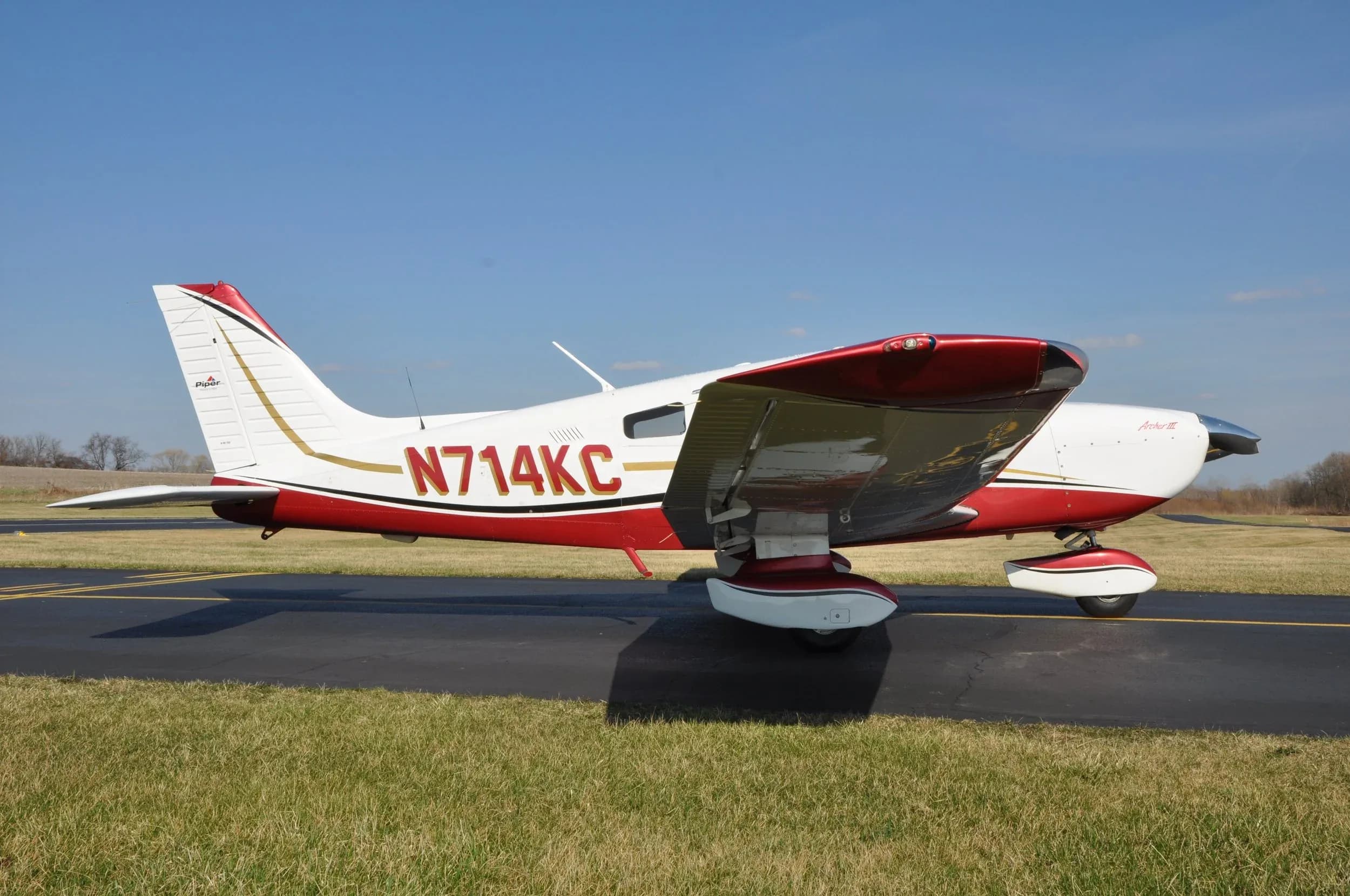 Piper Archer III aircraft with a white and red paint scheme on the tarmac.