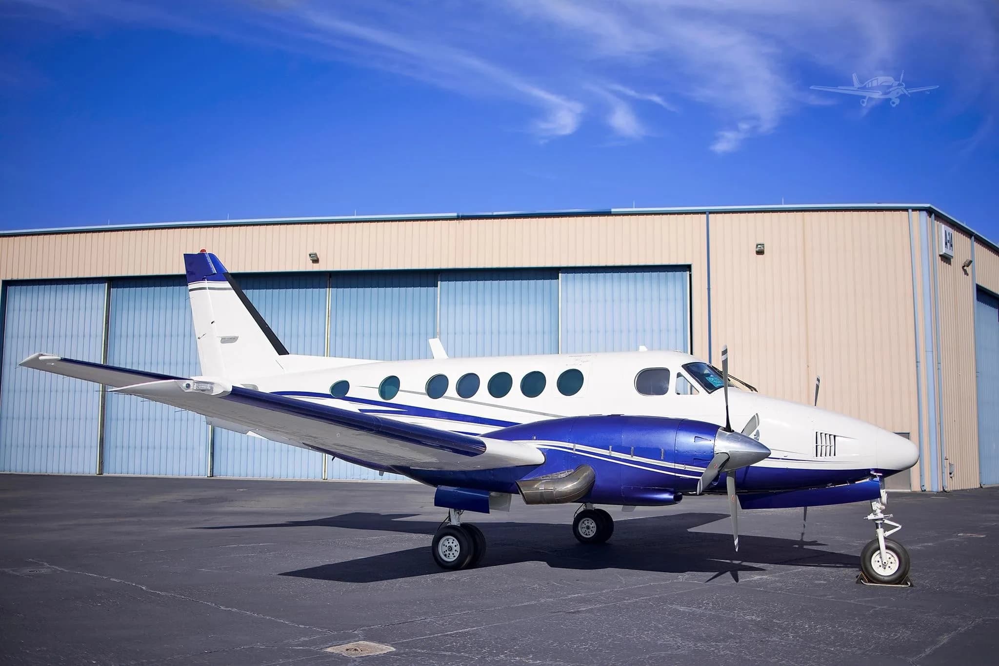 A white and blue twin-engine turboprop aircraft (Beechcraft King Air) with registration N222LP parked on an asphalt ramp in front of a large hangar.