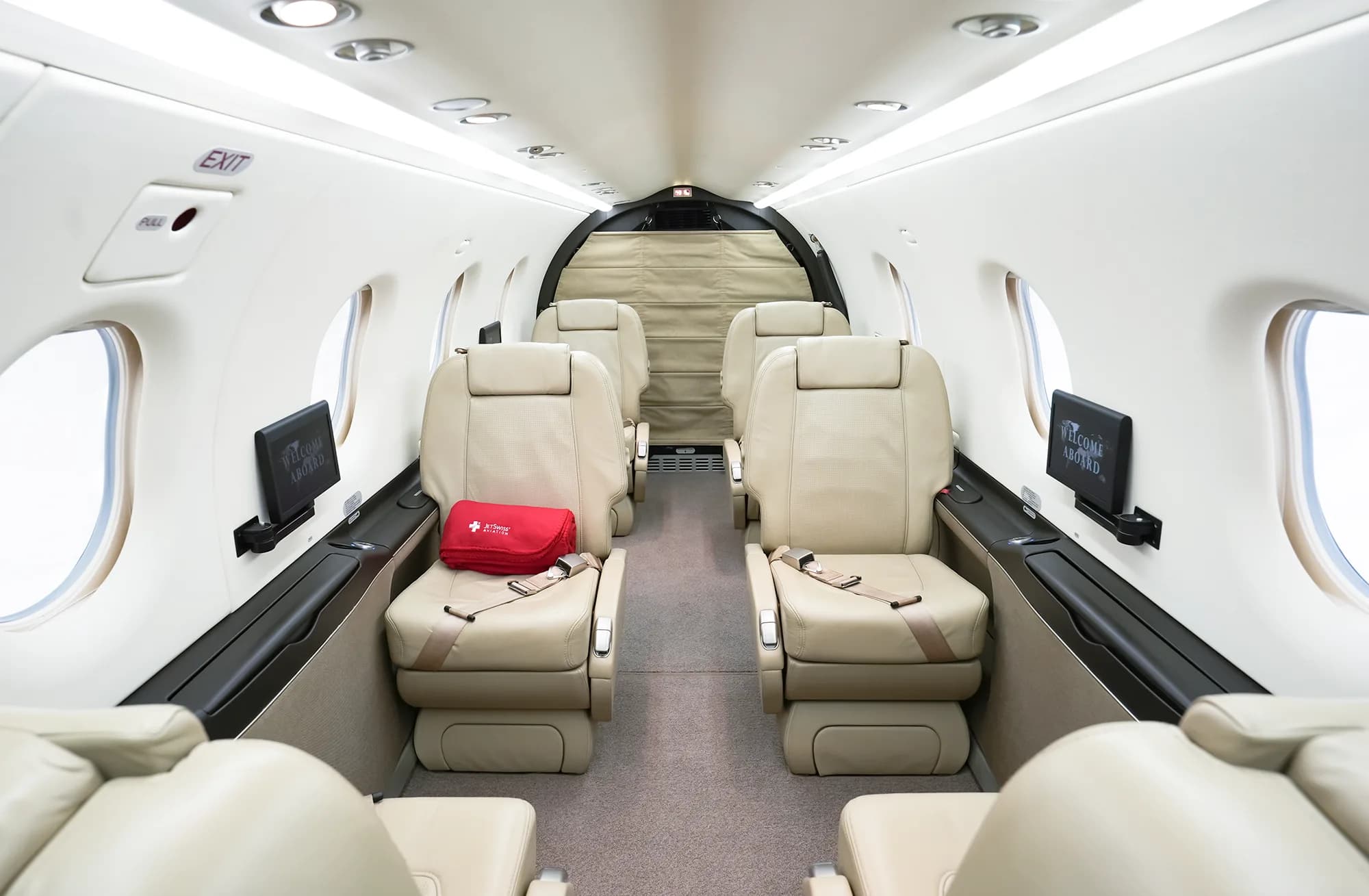 The aircraft cabin interior features beige leather seats arranged in a club configuration, looking towards the rear.