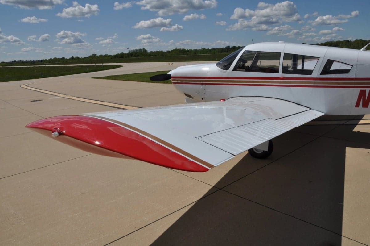 A close-up view of the right wing and front fuselage of a white aircraft with red and gold stripes.