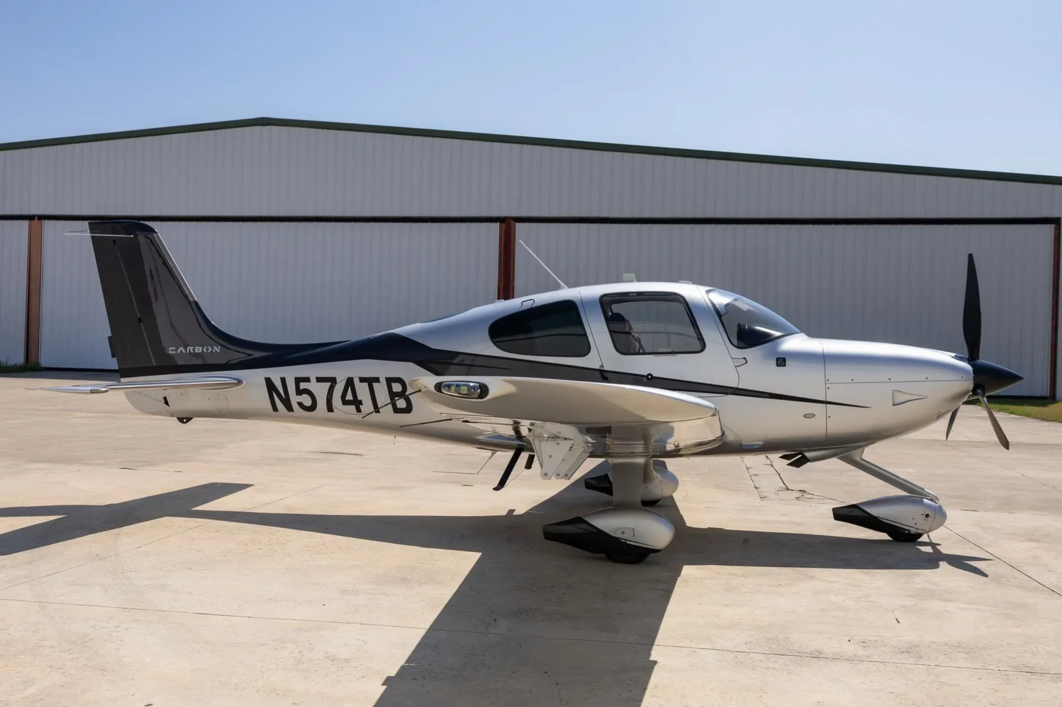 A side view of the silver and black Cirrus SR22 aircraft, registration N574TB, parked on a concrete apron.