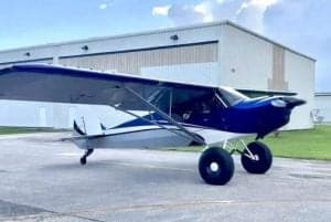 A blue and white aircraft is parked on the tarmac in front of a hangar.