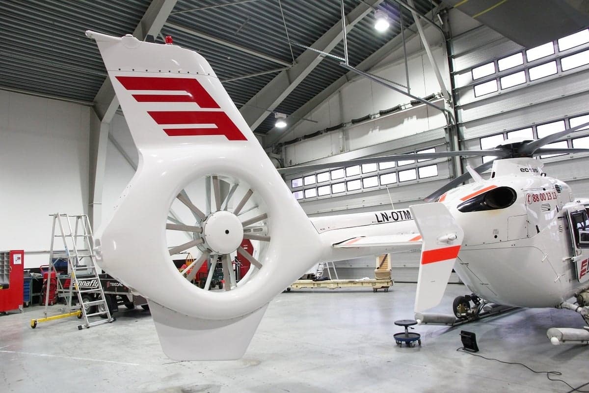 The tail rotor and fuselage of a white EC135 helicopter in a hangar.