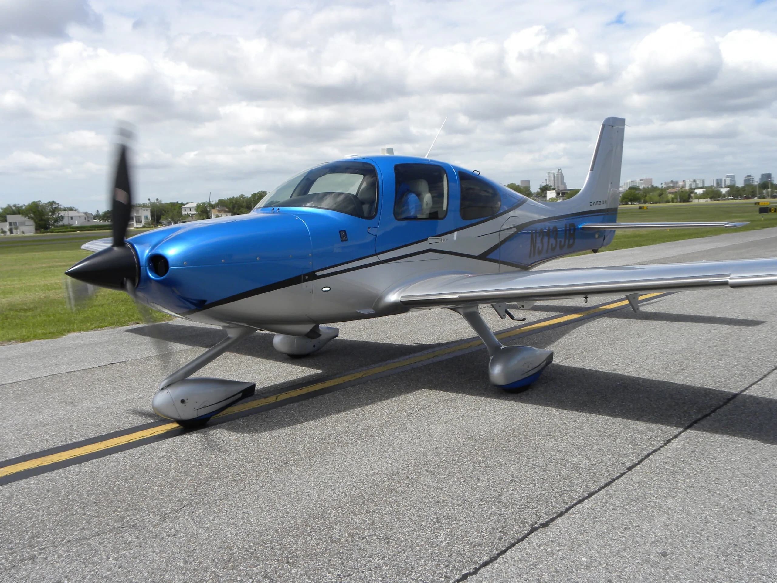 A blue and silver Cirrus SR22T aircraft, N313JB, with its propeller spinning on an airport taxiway.