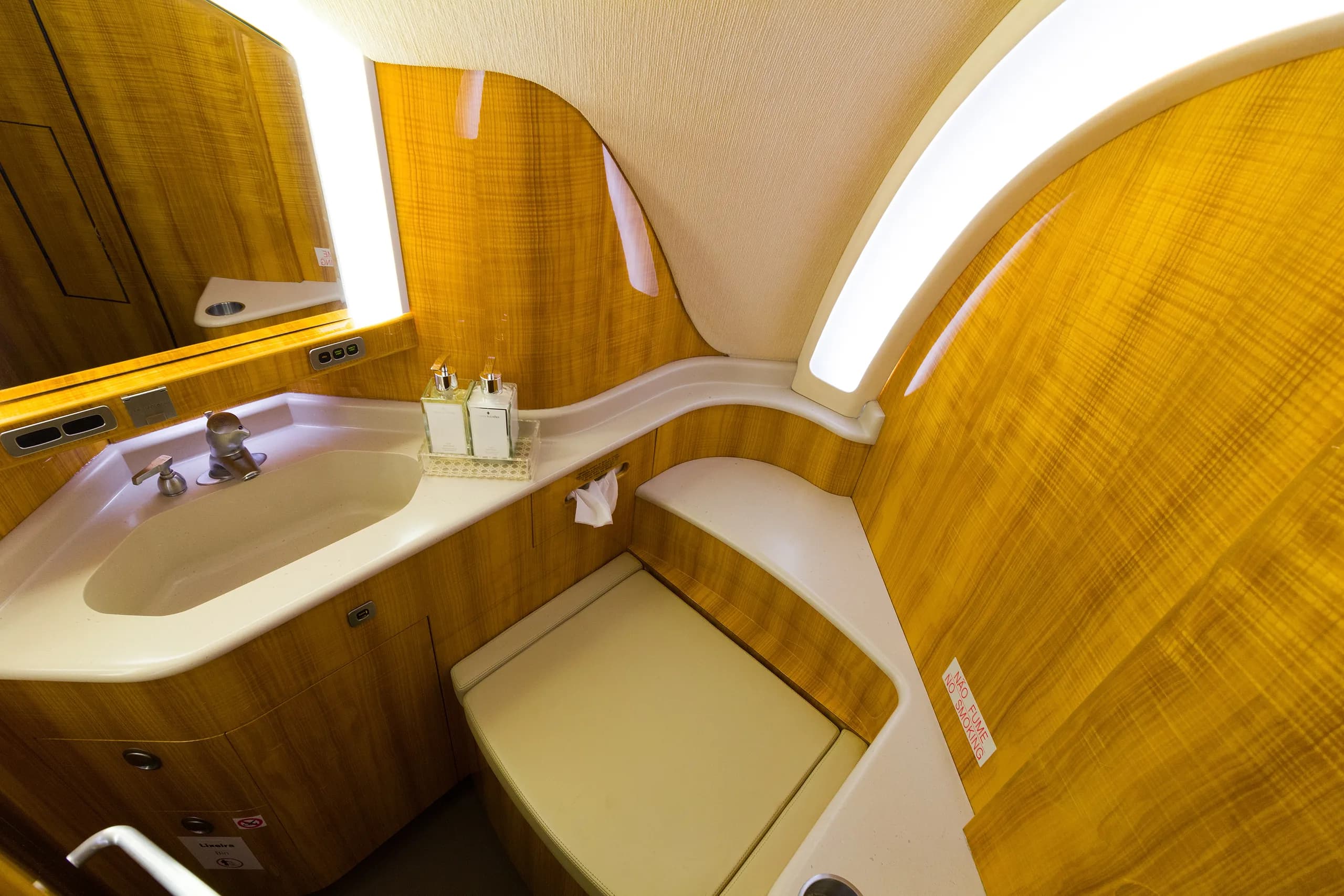 The private jet lavatory with a sink, mirror, and toilet, all featuring polished wooden walls.