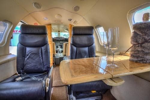 The Learjet 31A cabin features black leather seats and a wooden table with champagne flutes.