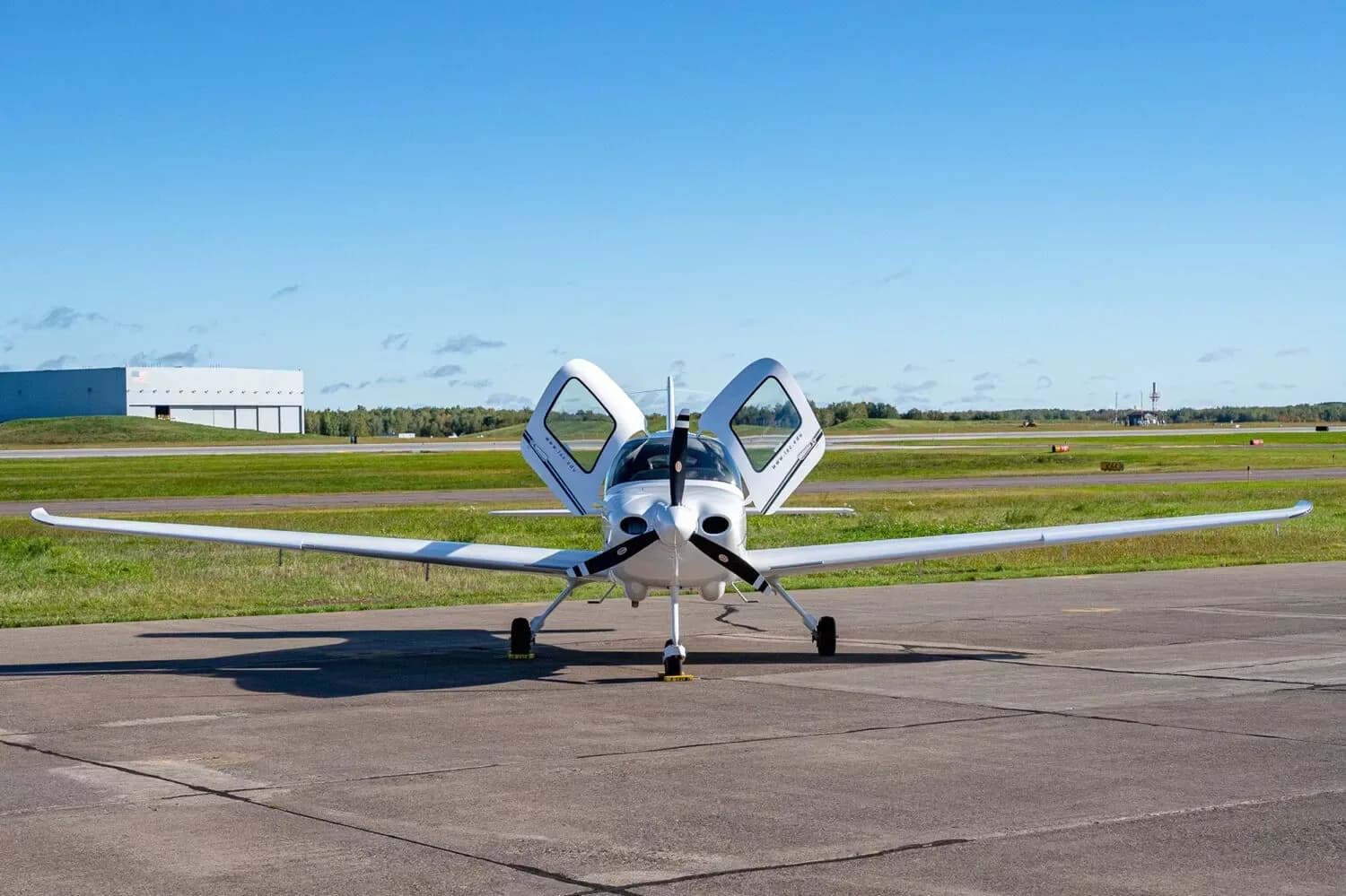 A white Cirrus SR20 aircraft with its doors open, viewed from the front, parked on an airfield.