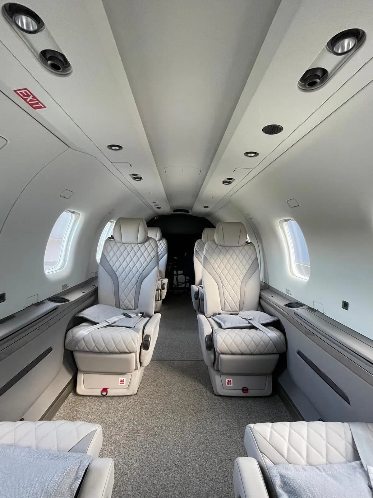 The luxurious light gray interior cabin of an aircraft features quilted leather seats and an "EXIT" sign.