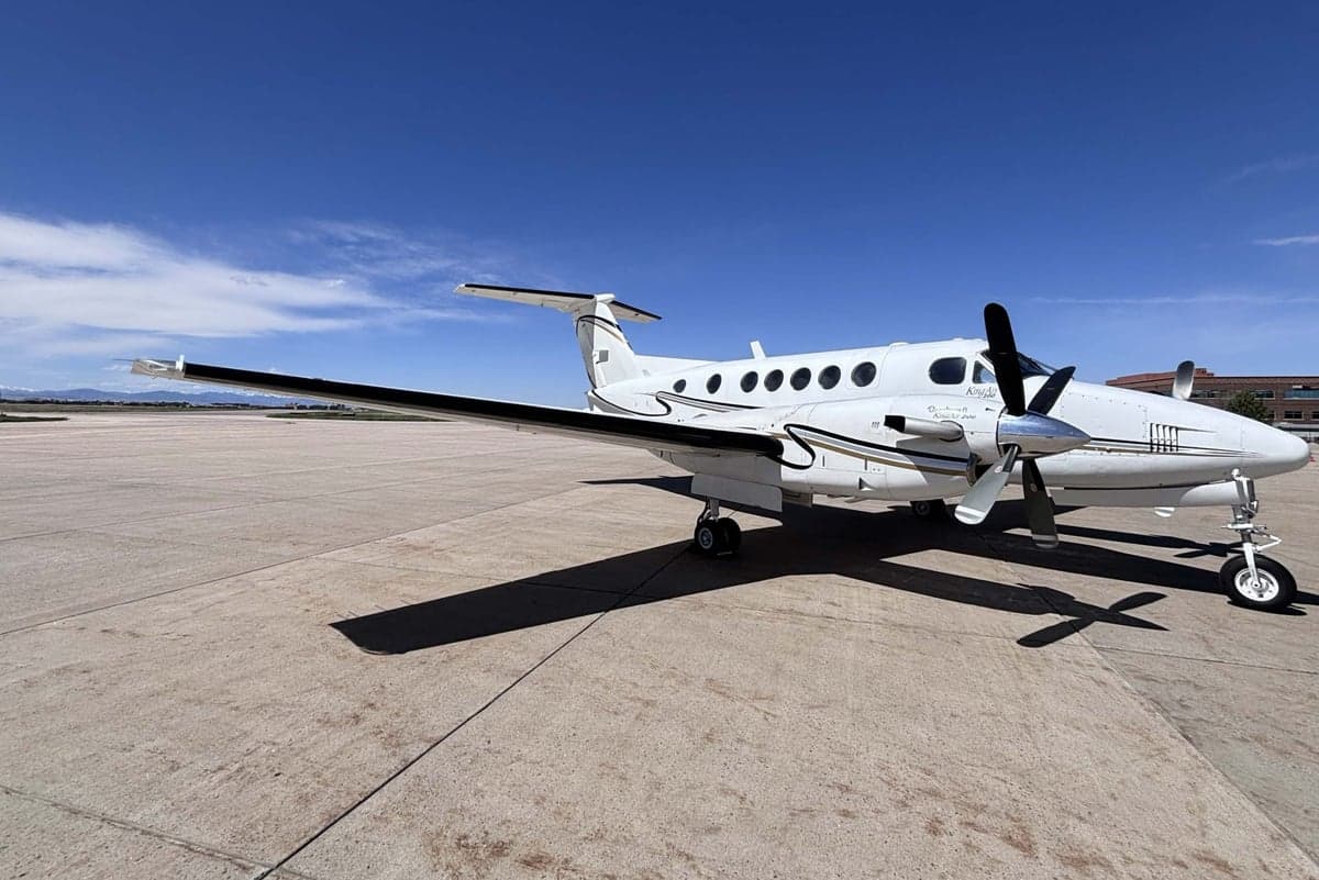 A white Beechcraft King Air N31WC with black and gold stripes parked on the tarmac.