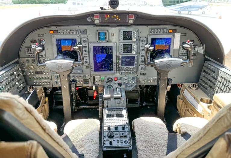 A wide view of the Cessna Citation CJ3 cockpit, showing the instrument panel with multiple displays, yokes, and center console.