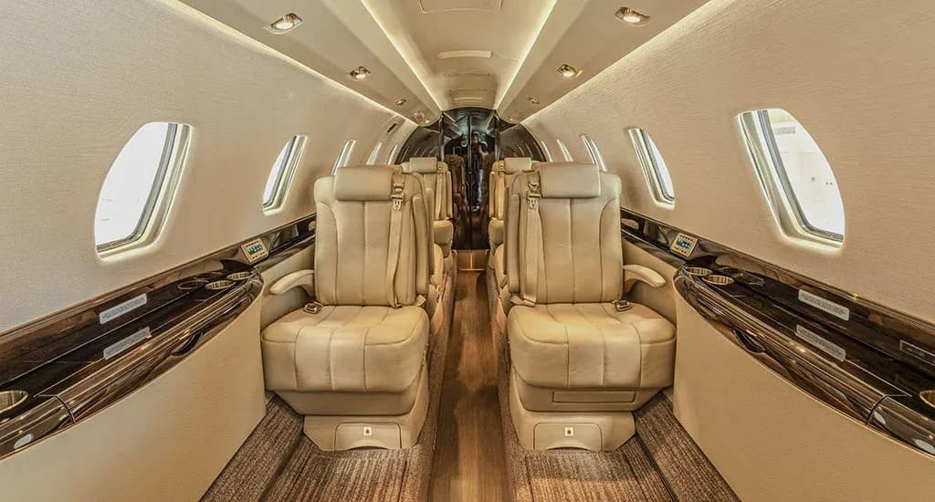 The luxurious interior cabin of a private jet with two rows of beige leather seats facing each other.