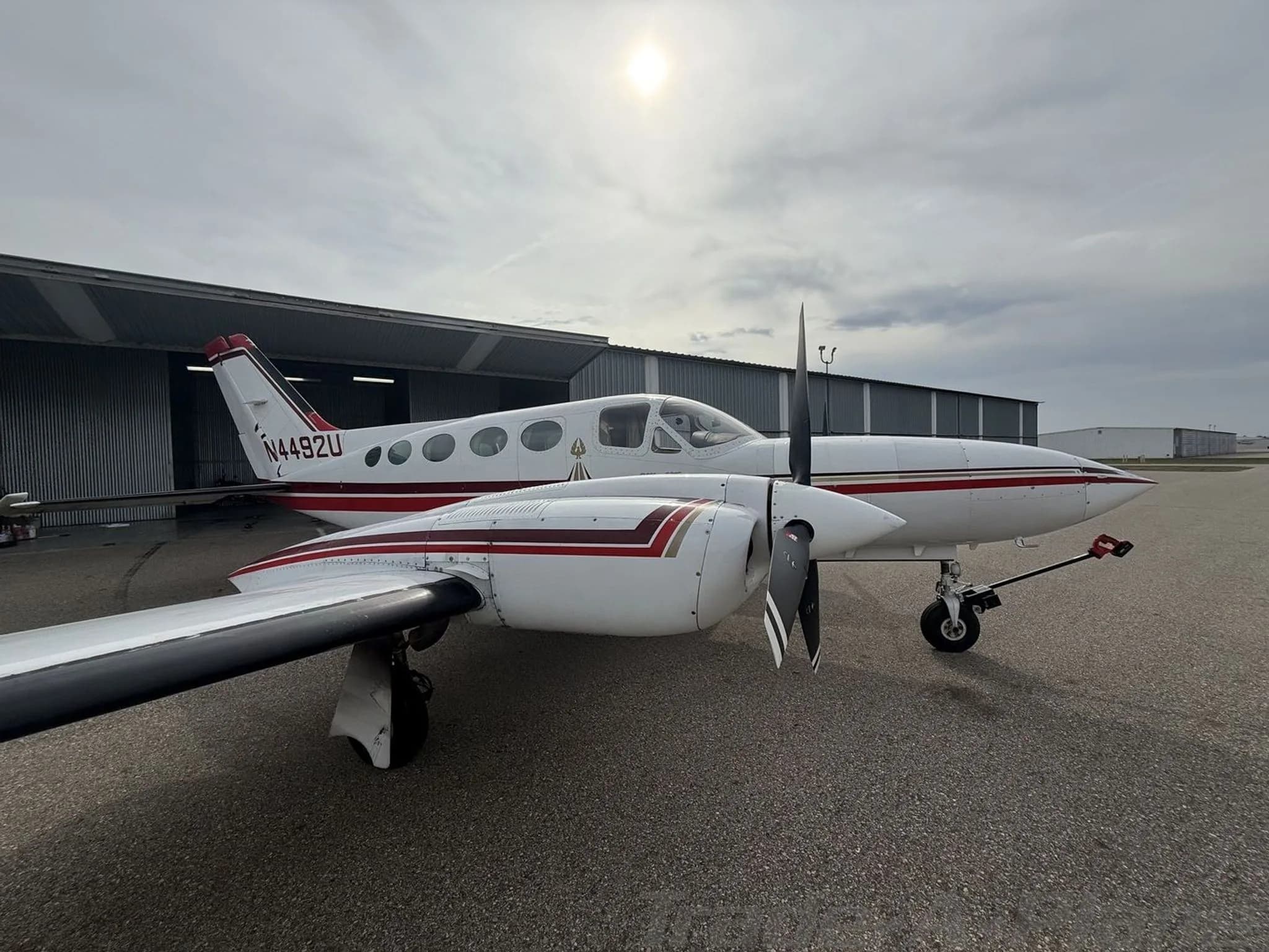 A side view of a white and red twin-engine Cessna 414 Chancellor aircraft, registration N4492U, parked on an asphalt ramp under a bright sky.