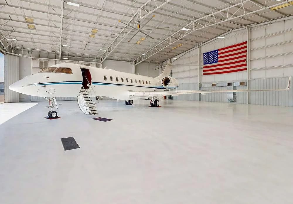 A white Bombardier Global Express business jet with blue stripes parked in a hangar with an American flag.