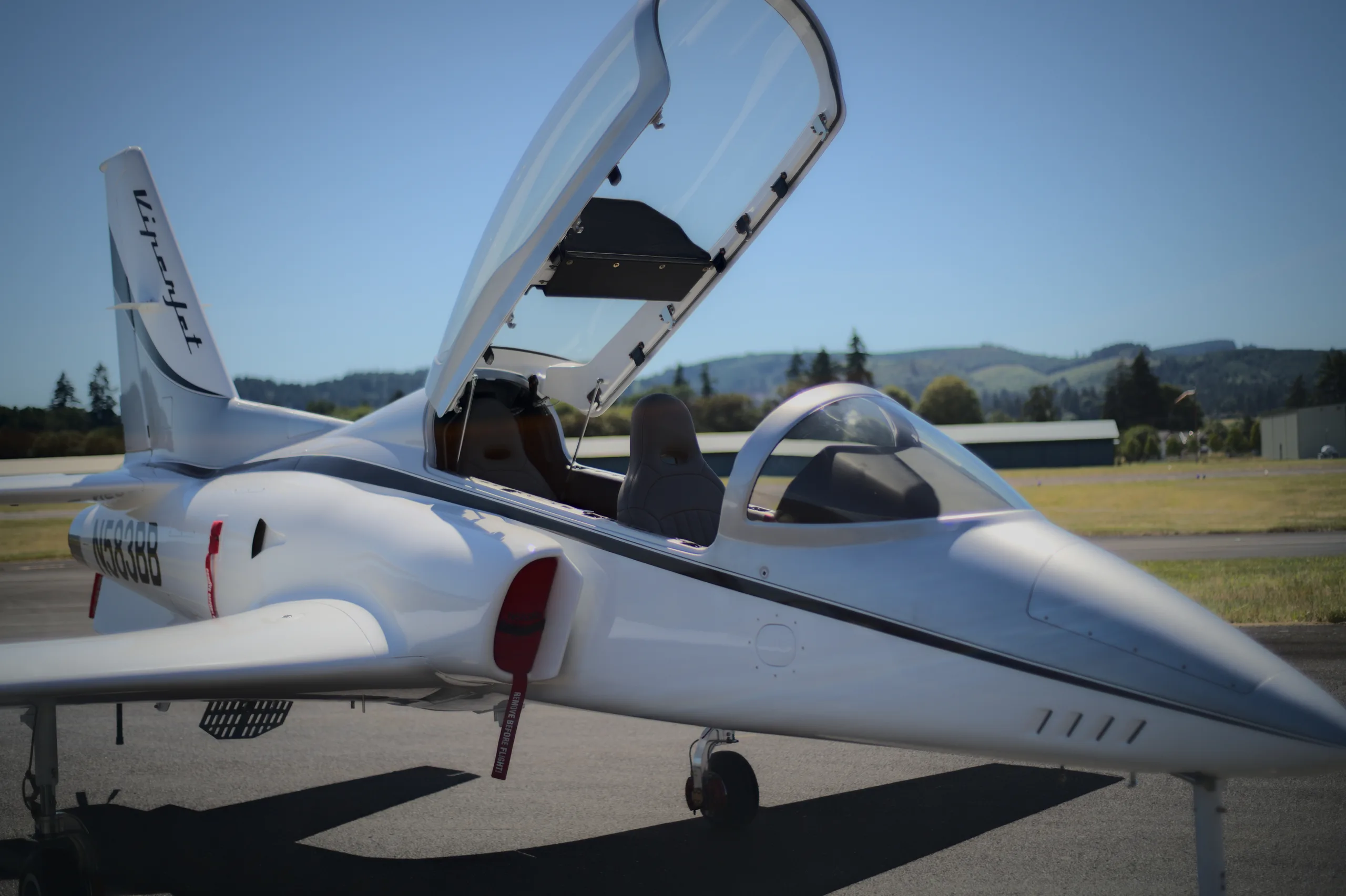 A white and silver Viperjet aircraft with its canopy open, parked on an airfield under a clear sky.