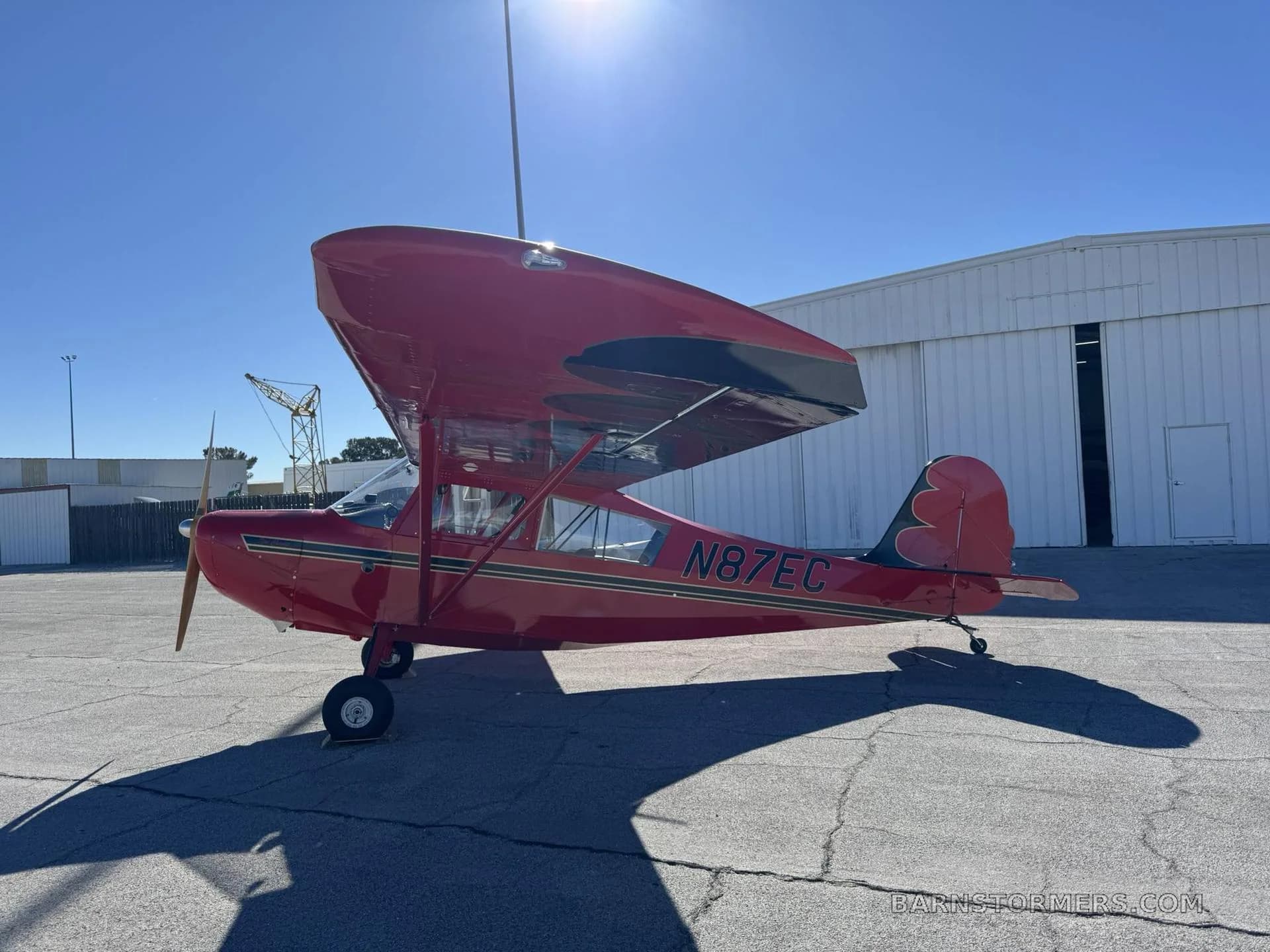 A red high-wing monoplane with registration N87EC is parked on an airfield, showing its right side and tail.