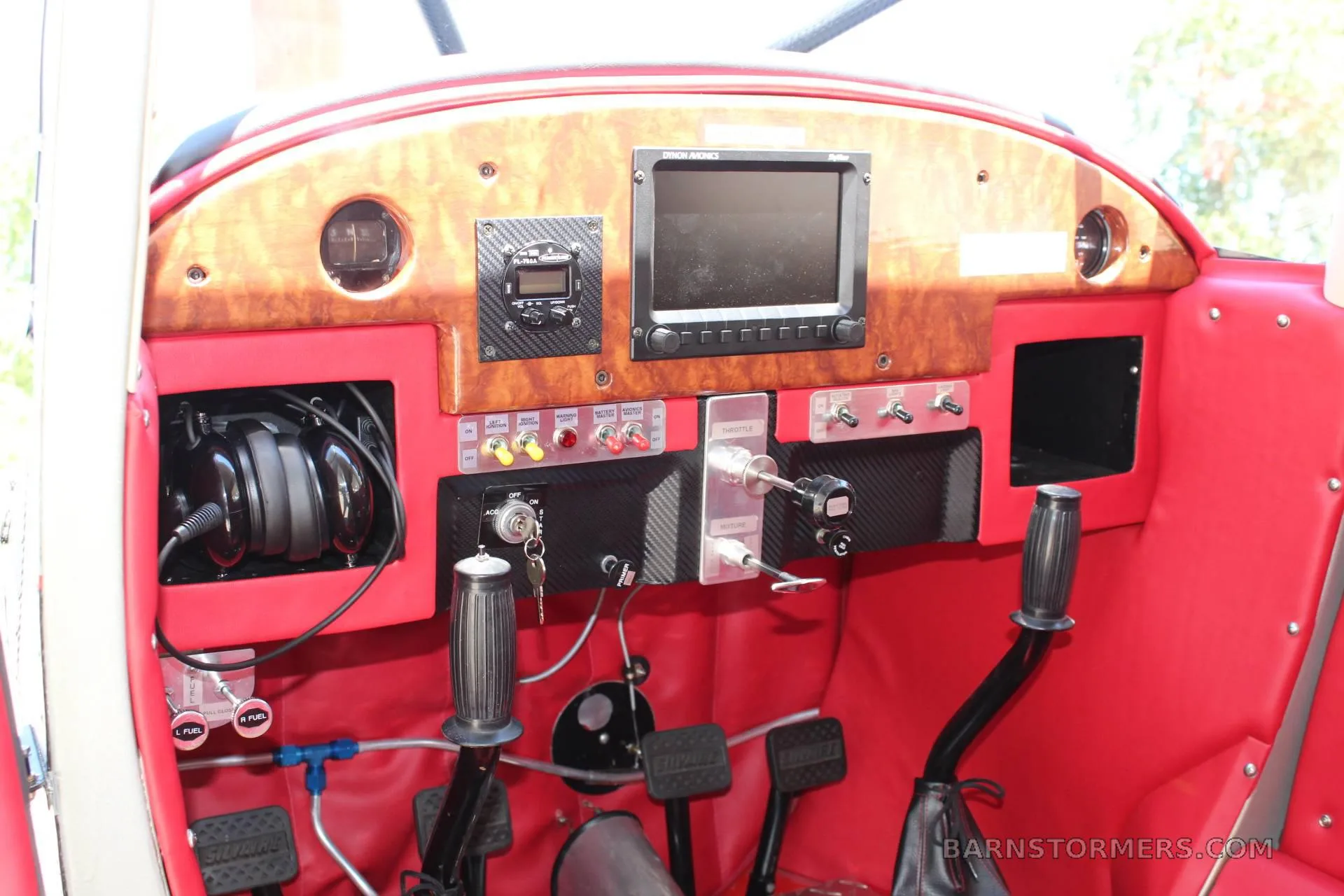 The cockpit of an aircraft with a wood-grain and carbon fiber instrument panel, red interior, and dual stick controls.