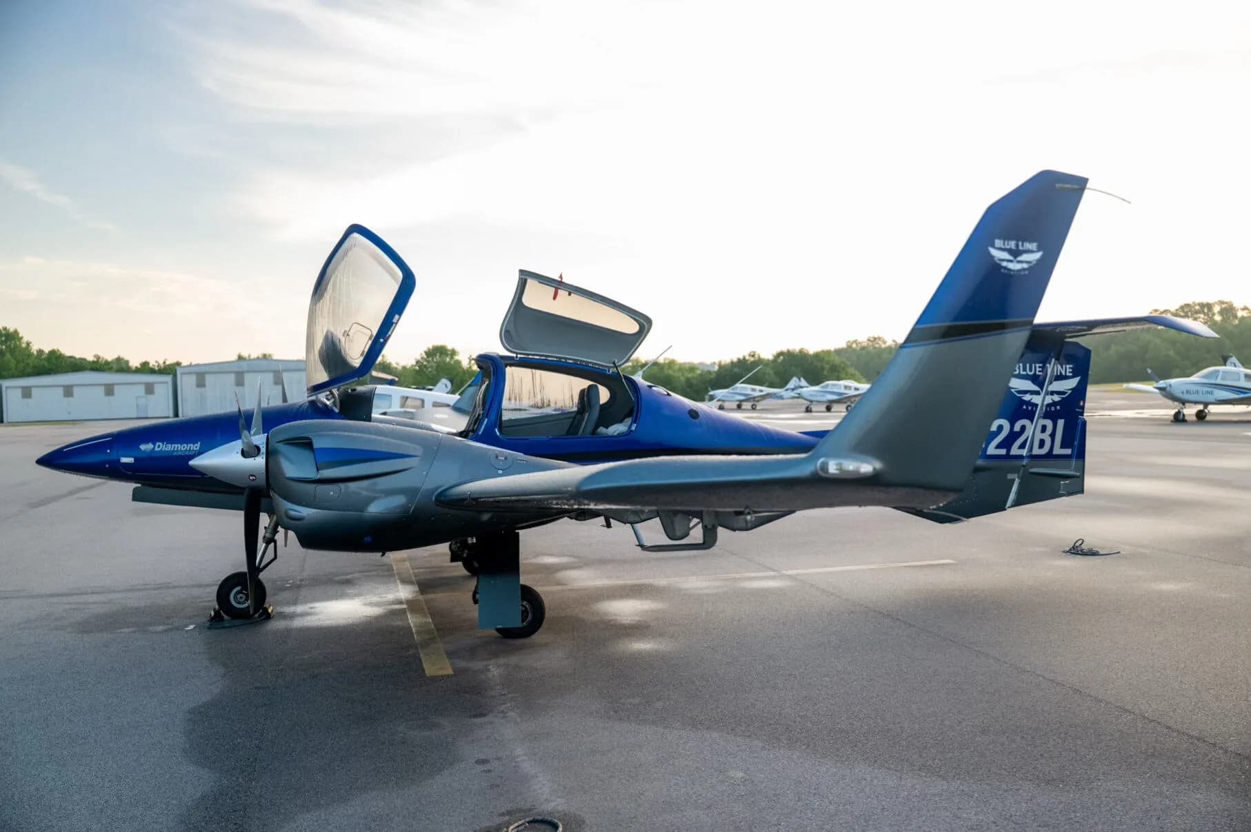 Side view of the blue and grey Diamond DA42NG aircraft, N422BL, with both canopy doors open on an airfield.