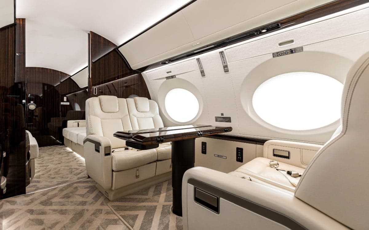 A view of the Gulfstream G500 cabin featuring cream-colored leather seats and a dark wood table.