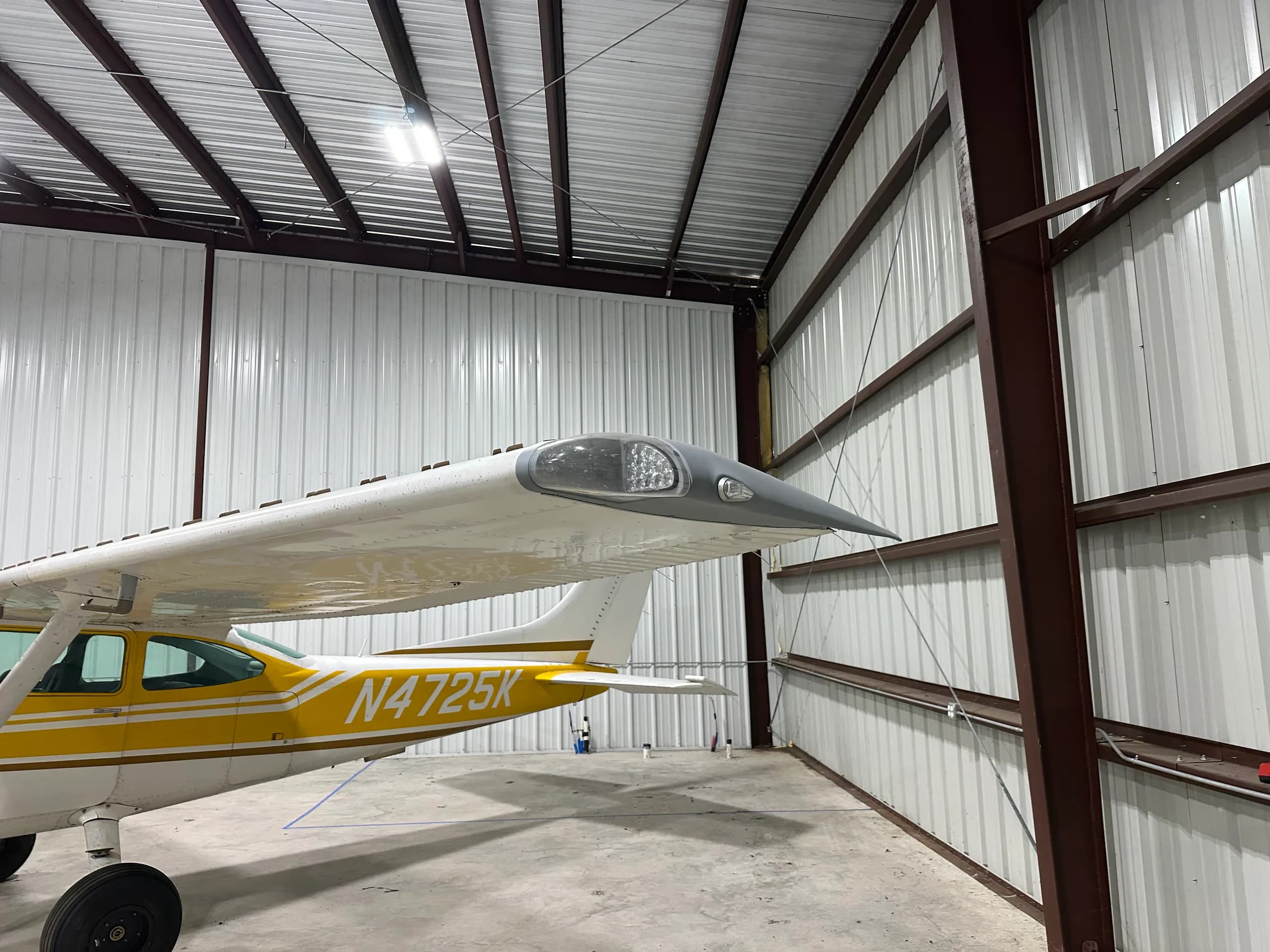 A close-up view of the right wingtip and fuselage of the yellow and white Cessna 172, N4725K, in a hangar.