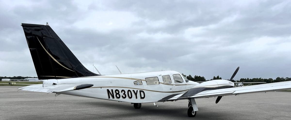 A Piper Seneca II aircraft with a white and black paint scheme is parked on the tarmac.