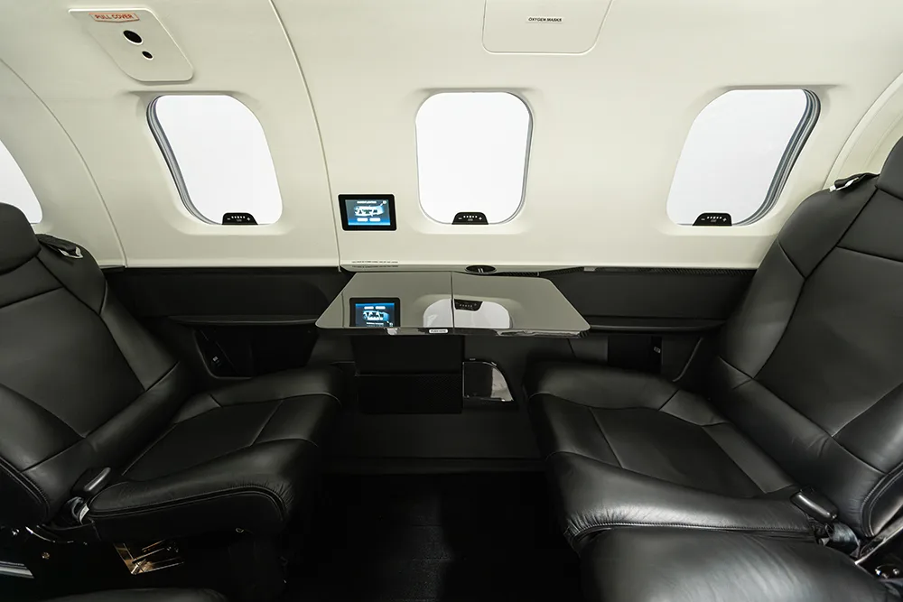 Two pairs of black leather seats facing each other with a small table in a private jet cabin.