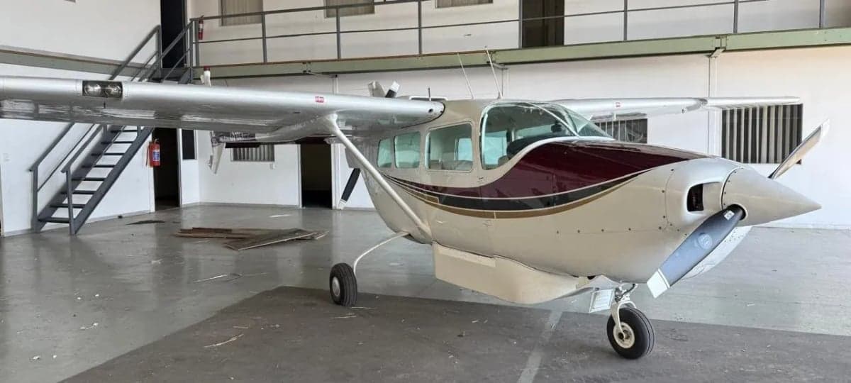 Side view of a white and maroon single-engine propeller aircraft with the propeller removed, parked in a hangar.
