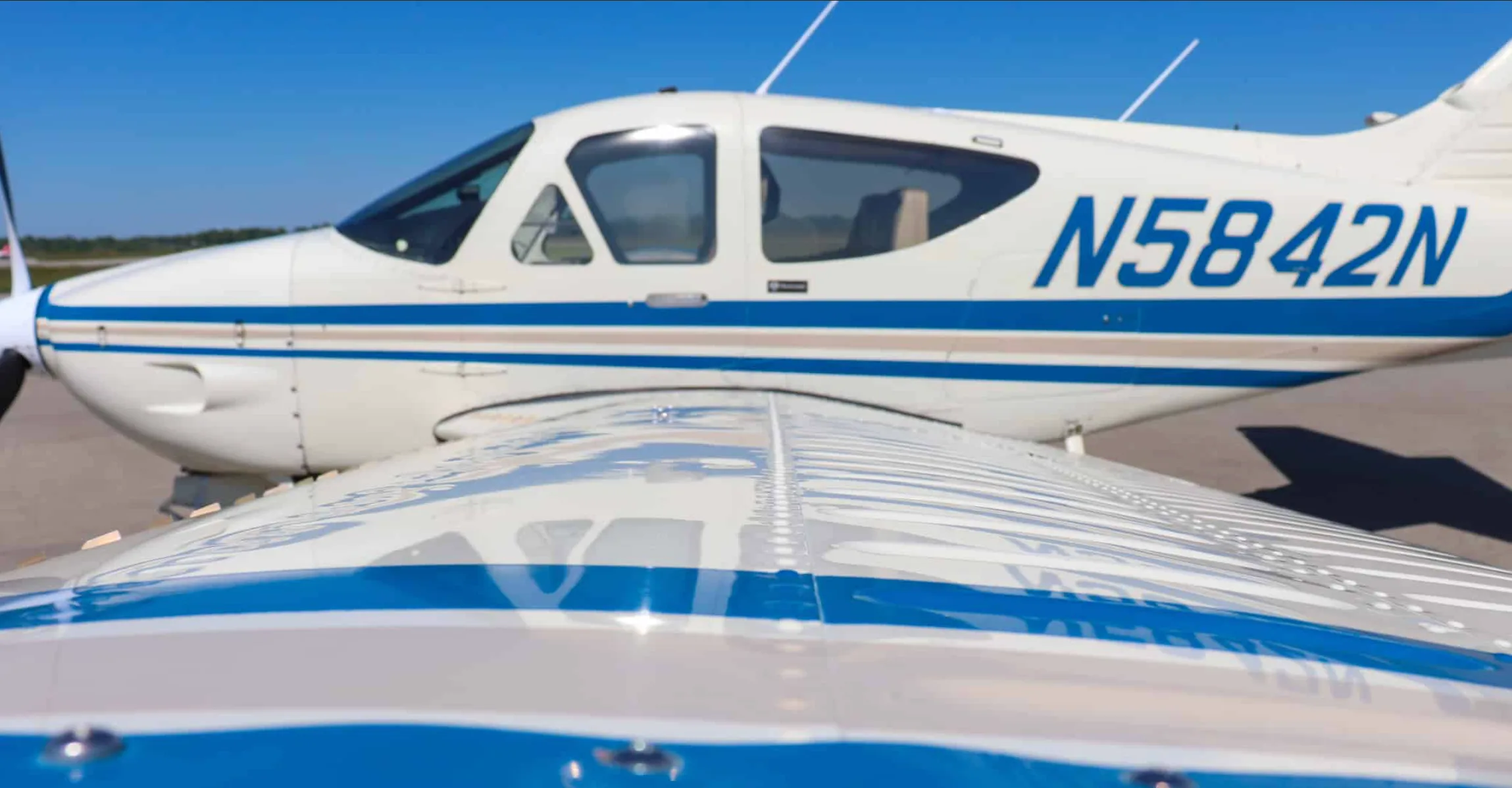 Close-up view of the wing and fuselage of a white aircraft with blue and tan stripes, showing registration N5842N.