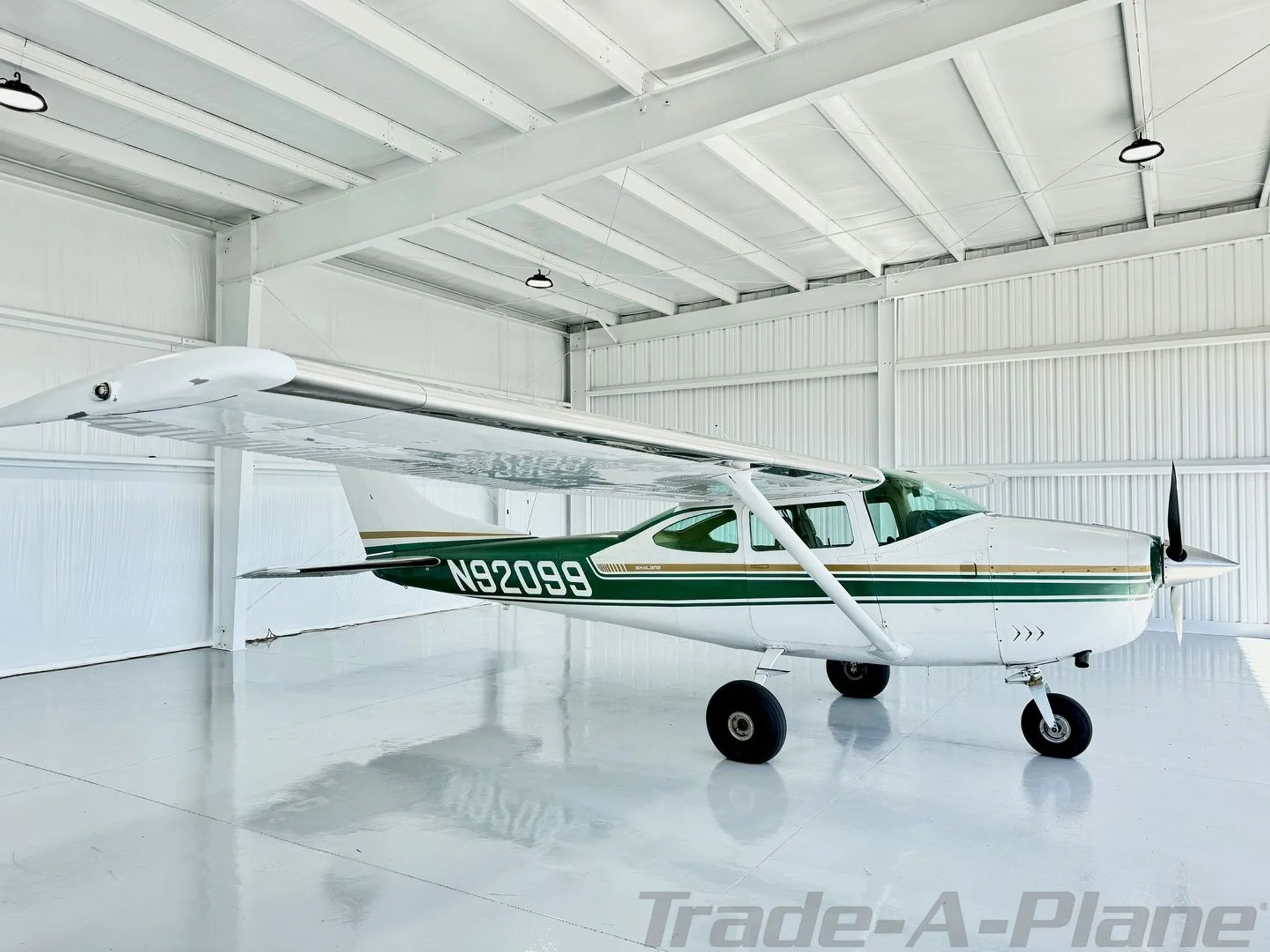 A white and green Cessna Skylane N92099 parked in a brightly lit hangar, viewed from the front-right.