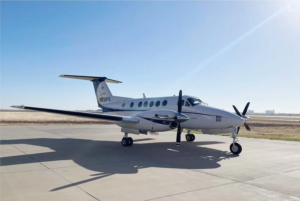 A white and blue twin-engine turboprop aircraft, N838PS, parked on an airfield under a clear sky.