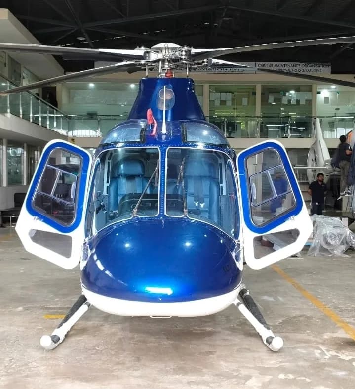 Front view of a blue and white helicopter with its cockpit doors open, revealing the blue seats inside.