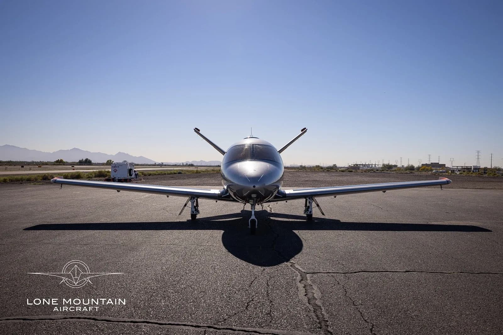 A head-on view of a silver Cirrus Vision Jet (SF50) with its wings extended, parked on an asphalt tarmac.