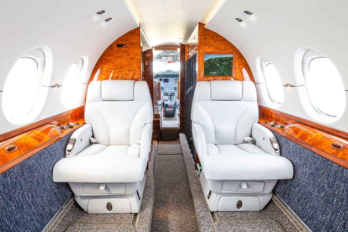 A view of the aircraft cabin, featuring white leather seats and wood trim.