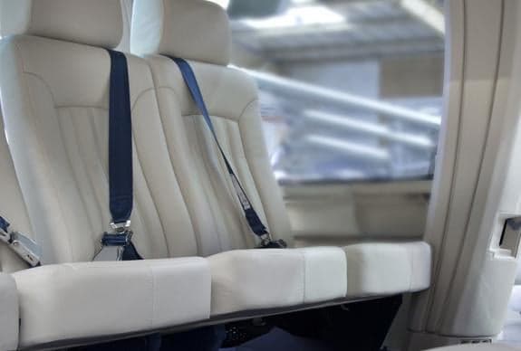 Close-up of the cream-colored leather seats with blue seatbelts in the helicopter cabin.