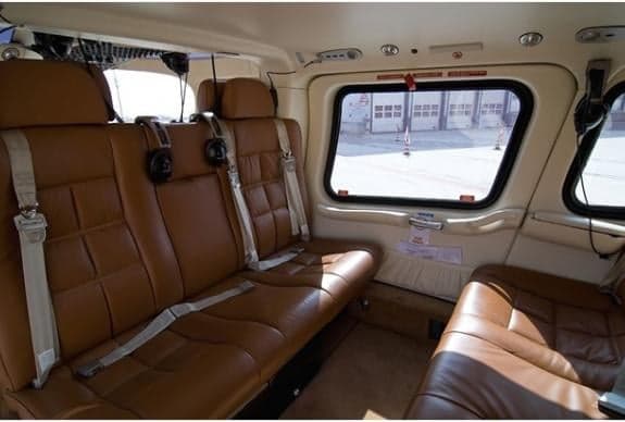 The interior of the helicopter features brown leather seats with white seatbelts.