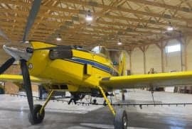A yellow Air Tractor aircraft parked inside a hangar, front view.